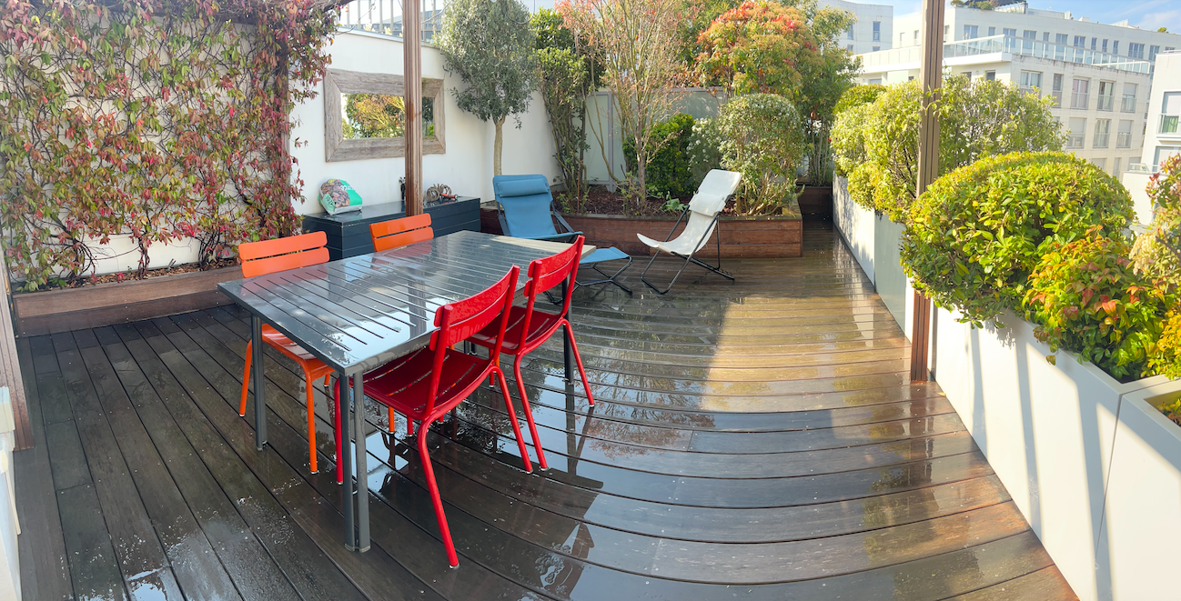 Terrasse en bois avec table et mobilier coloré, entourée de végétaux